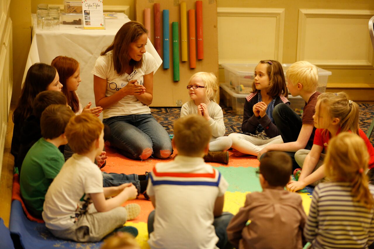 Children sit around a mat interacting with their teacher.