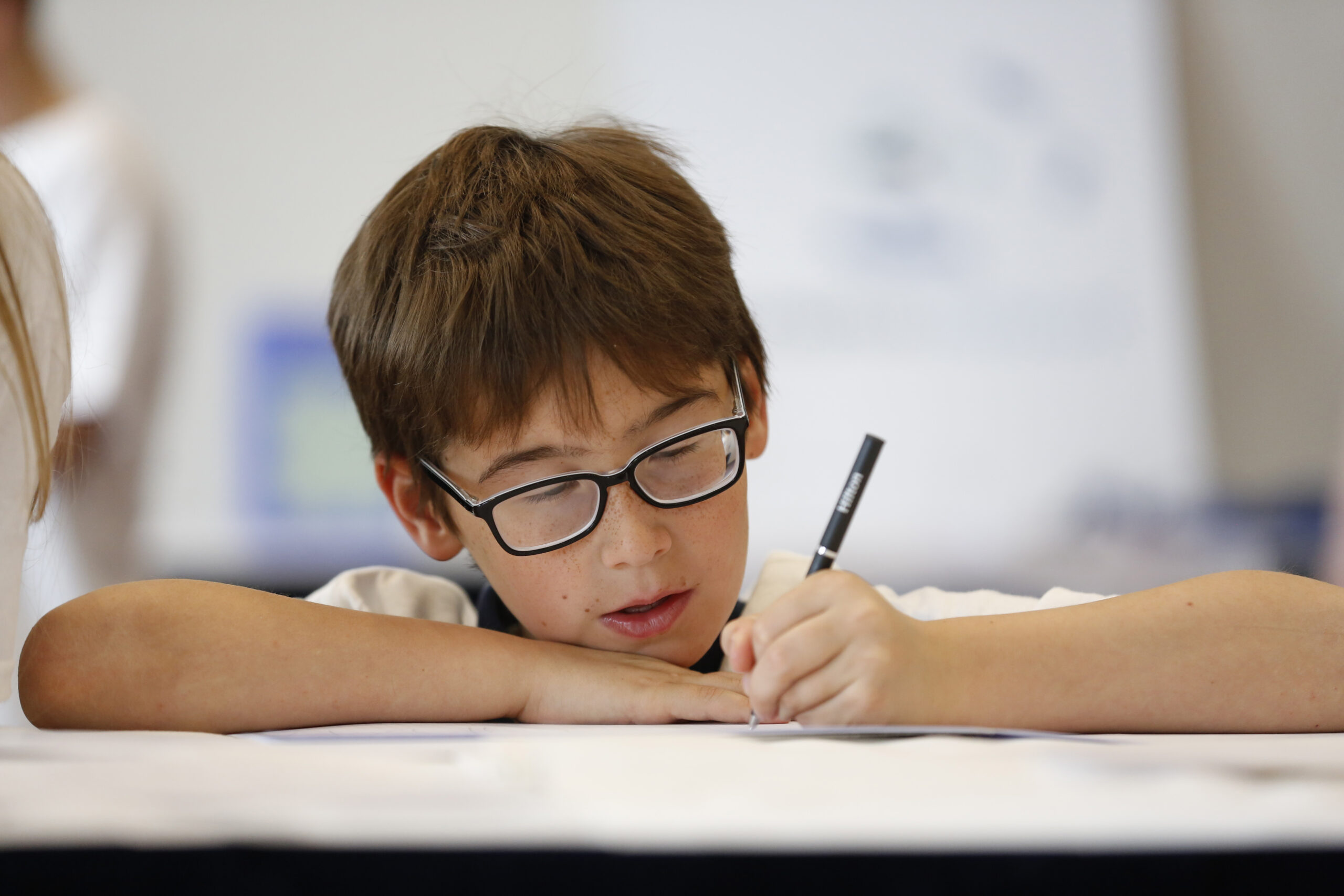 A boy wearing glasses, writing.