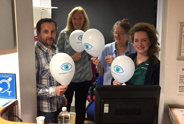 People stand at a clinic reception holding Nystagmus Network balloons.