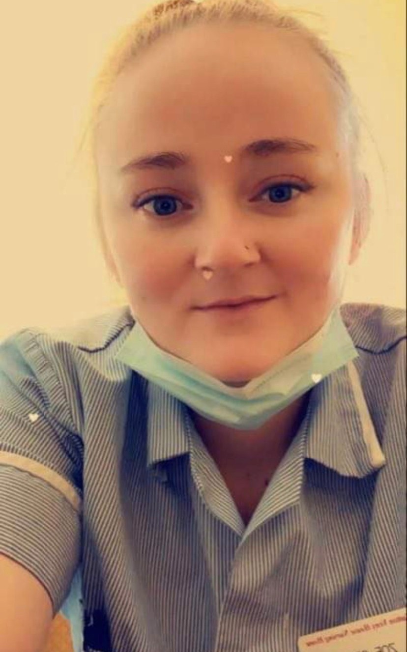 Zoe wears a care worker's uniform and a face mask pulled down under her chin for the photo.