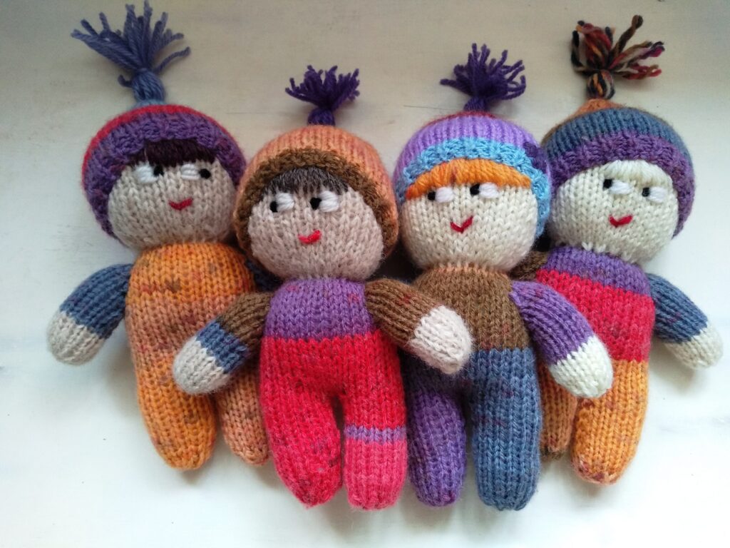 4 woolly knitted nystagmus mascots, wearing brightly coloured onesies and hats with tassels.