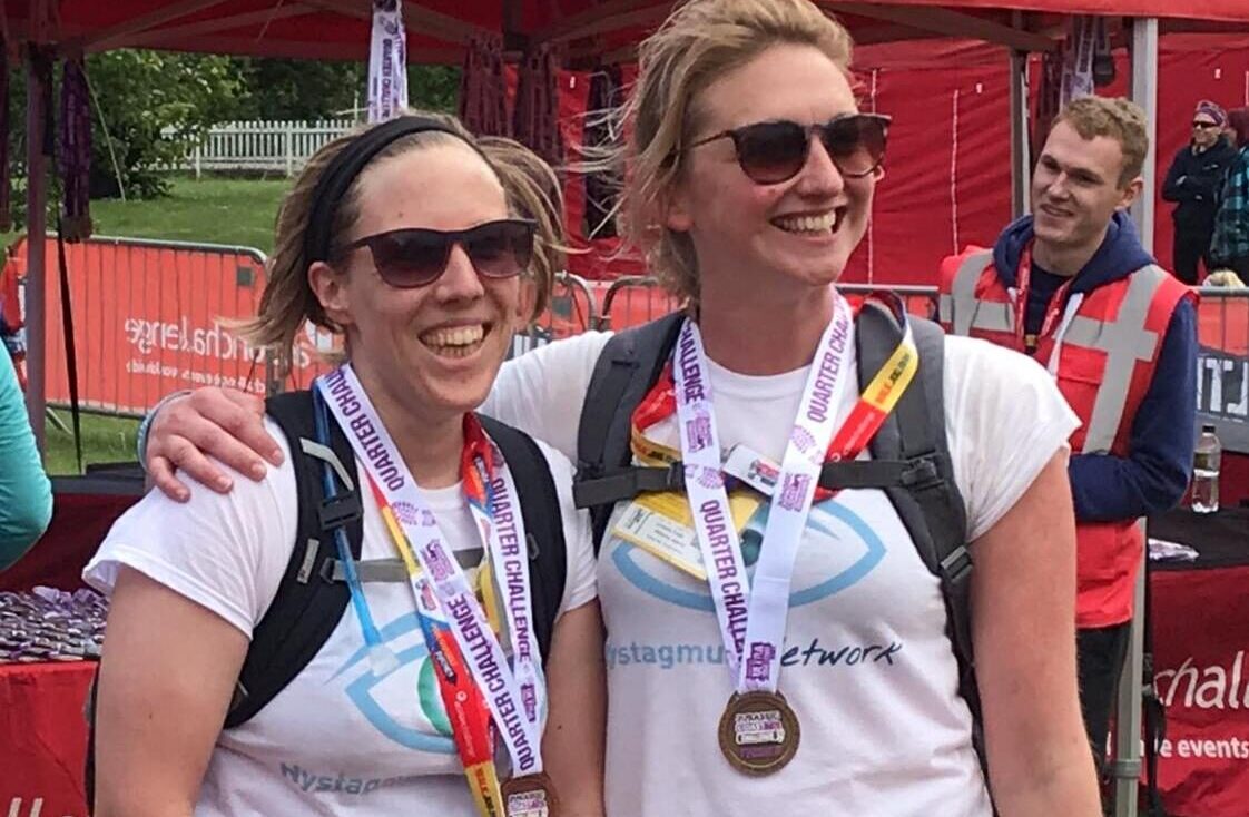 2 runners in Nystagmus Network T-shirts wearing their finishers' medals