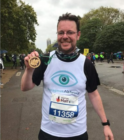 Stephen wearing a Nystagmus Network running vest and holding his finisher's medal.