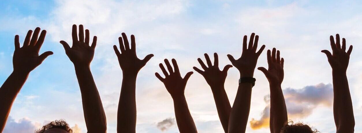 Raised hands silhouetted against a blue sky.