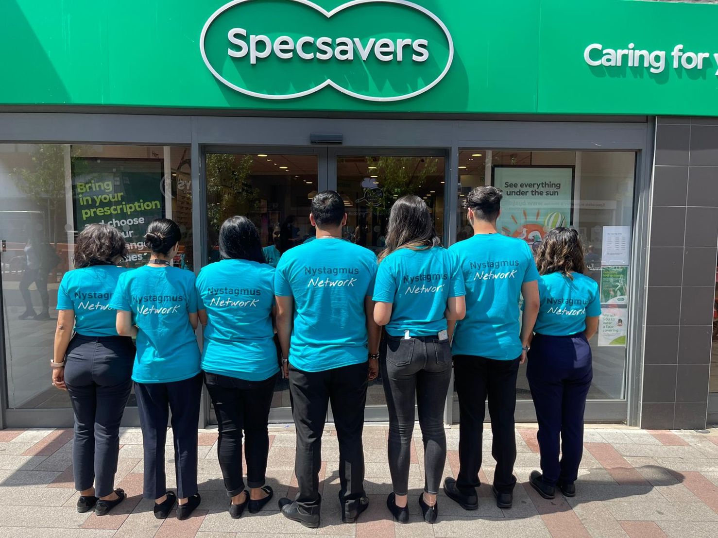 A row of people stand outside Specsavers wearing Nystagmus Network T-shirts.
