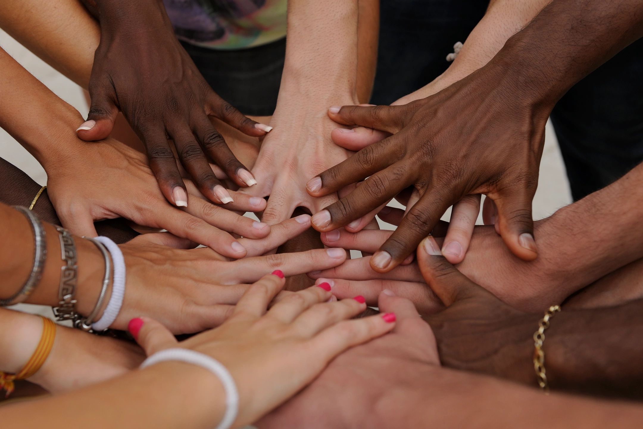 A group of hands reaching in together, wearing charity wrsitbands.