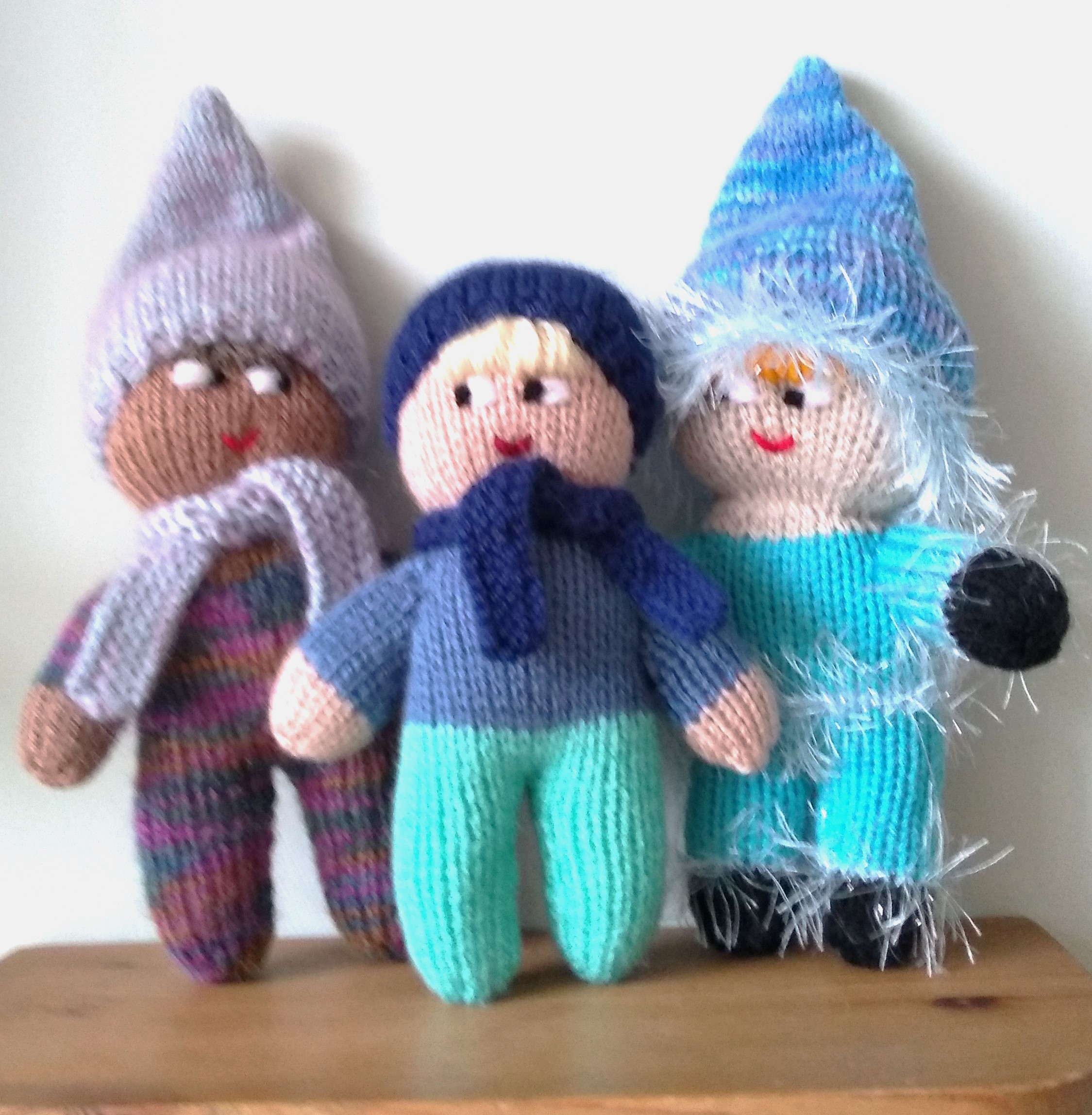 Three knitted mascots standing on a shelf.