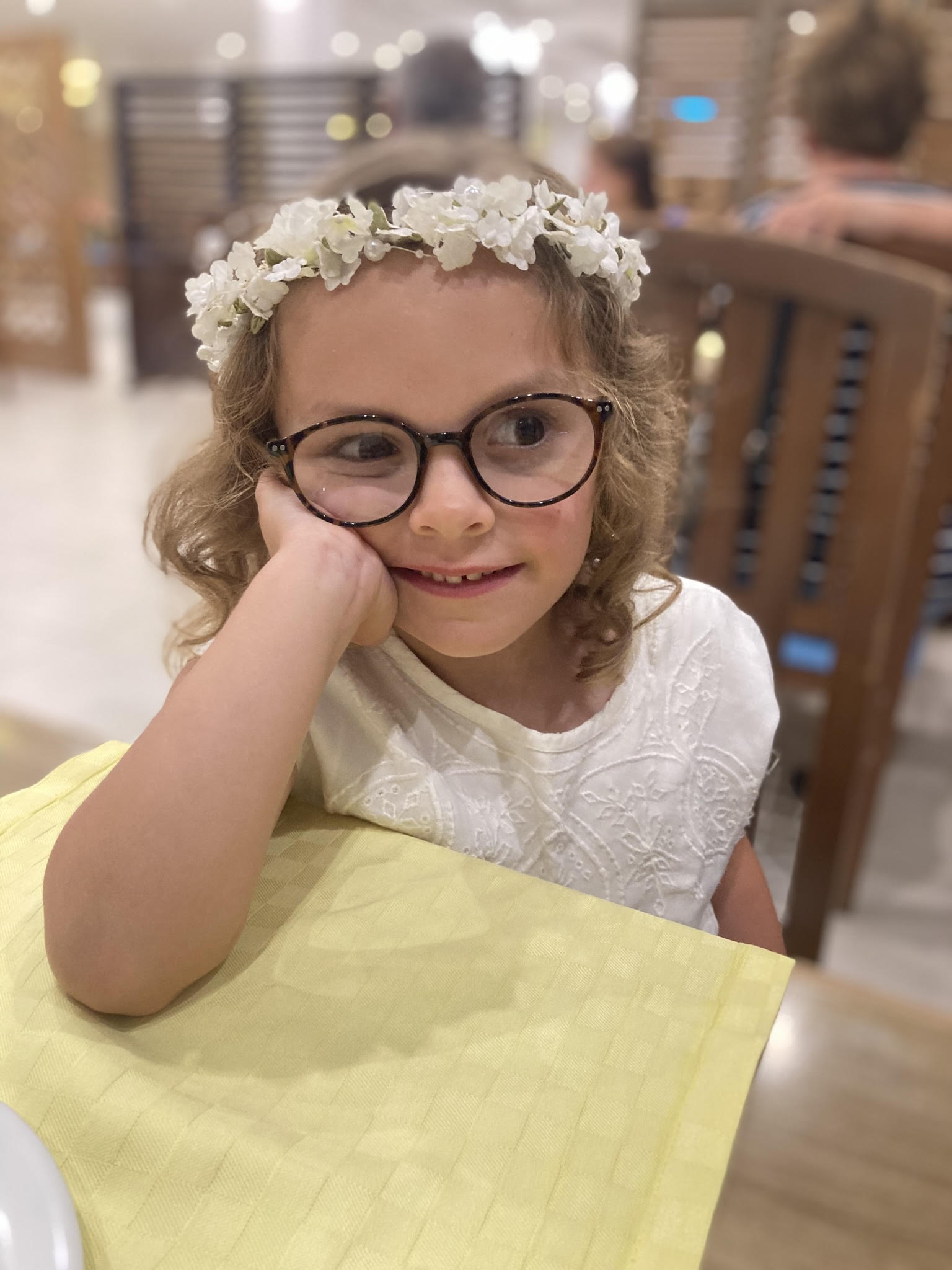 Claudia wears a white top, glasses and a floral crown.