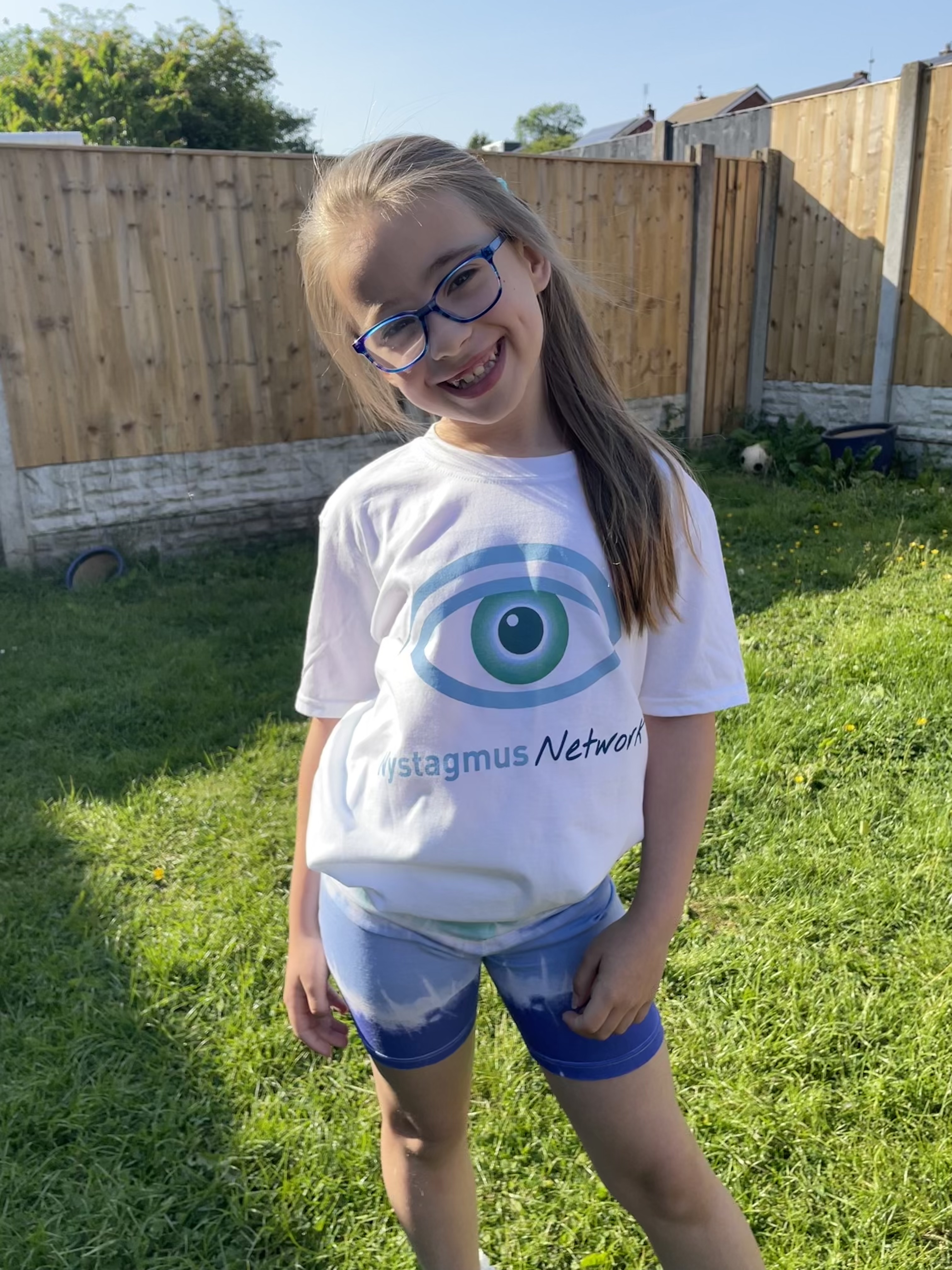 Robyn stands in a garden, wearing a Nystagmus Network T-shirt.