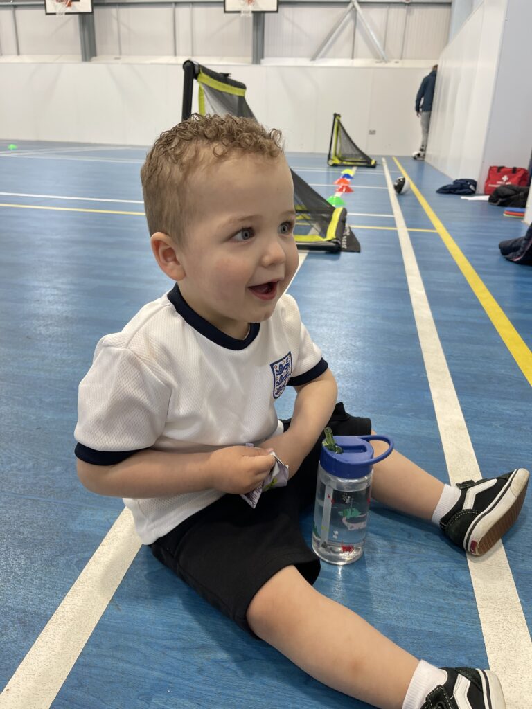 Mason is sitting on the floor of a sports hall holding a water bottle.