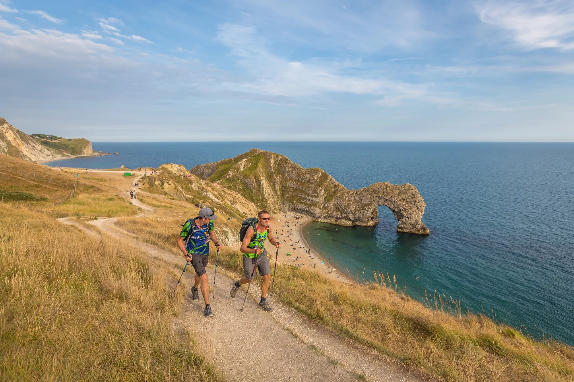 Two walkers with poles on the Jurassic coast path with the sea in the background.