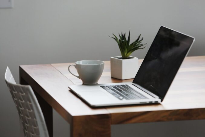 A desk with an open laptop, plant and coffee cup.