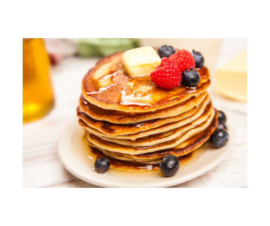 A stack of pancakses on a plate topped with butter, strawberries and blueberries.