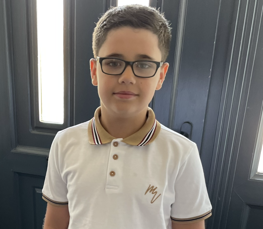 Cohen smiling for the camera, wearing glasses and a white polo shirt with a black striped collar