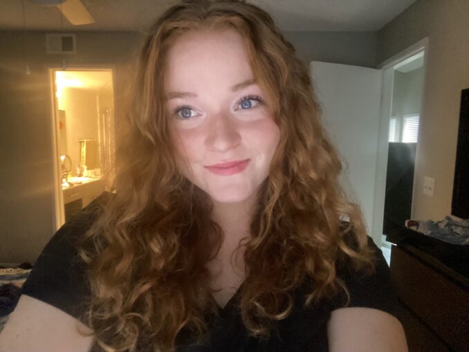 A young woman with long, wavy 'red' hair smiles for the camera.