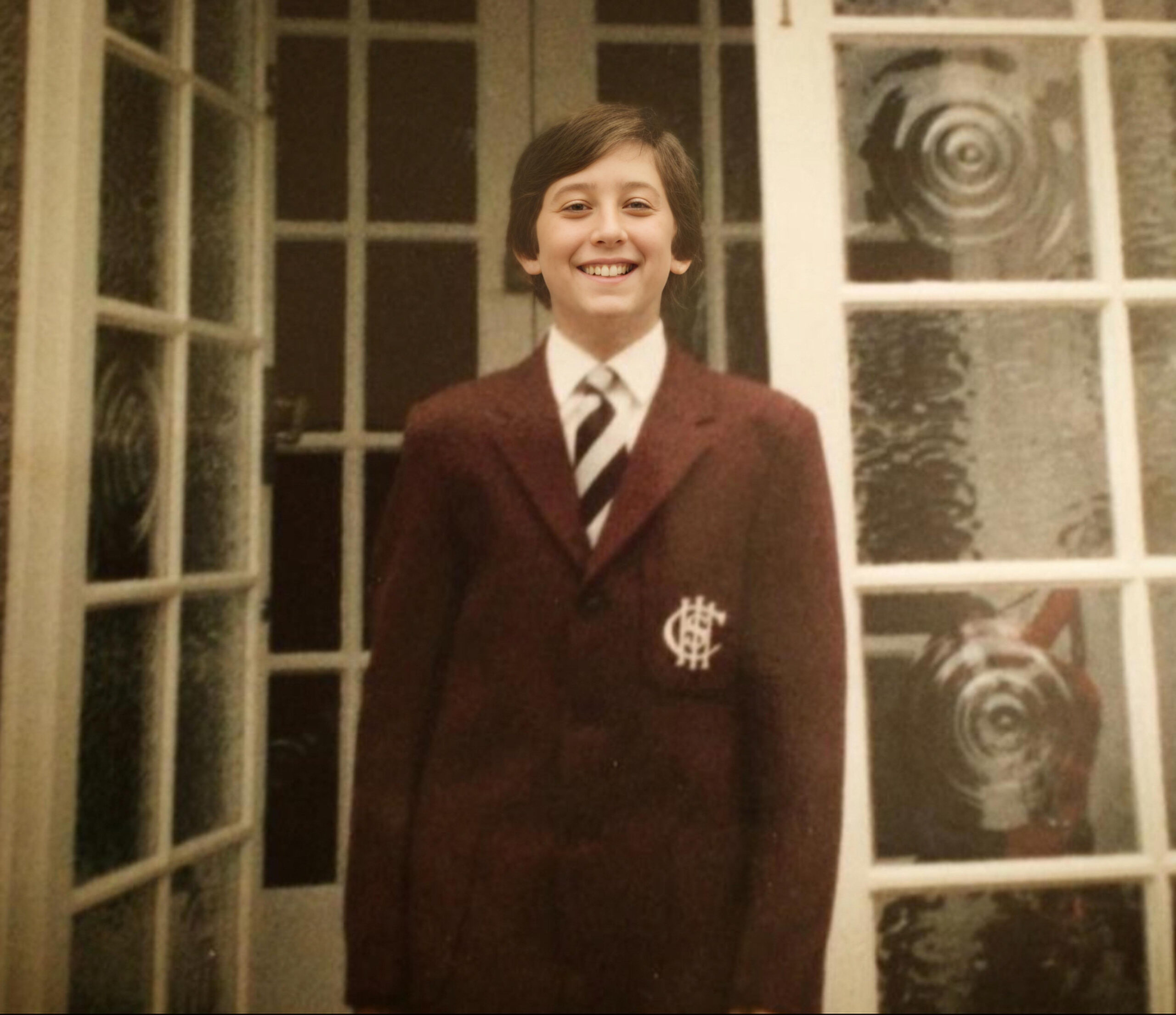 Paul is proudly smiling for the camera wearing a smart burgundy coloured school uniform.
