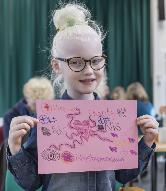 A child wearing glasses is holding up a poster she has made.