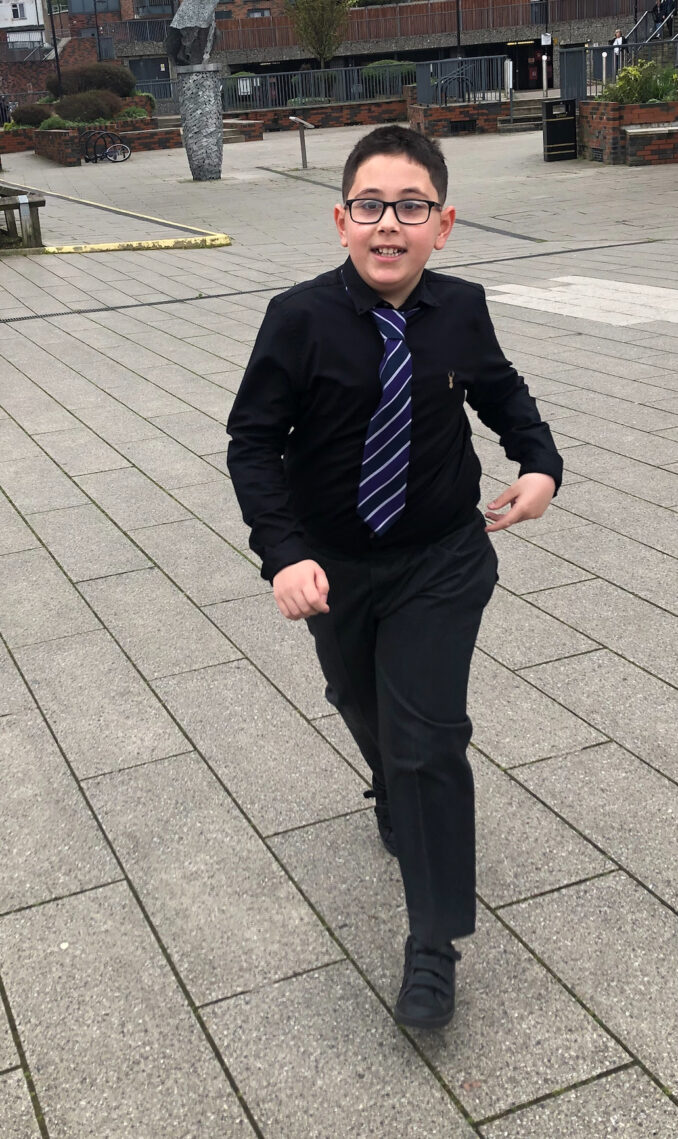 Taylan is wearing a smart suit with a striped tie. He is smiling for the camera and standing outside in an open space.