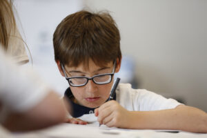 A boy wearing glasses is writing with a pen.