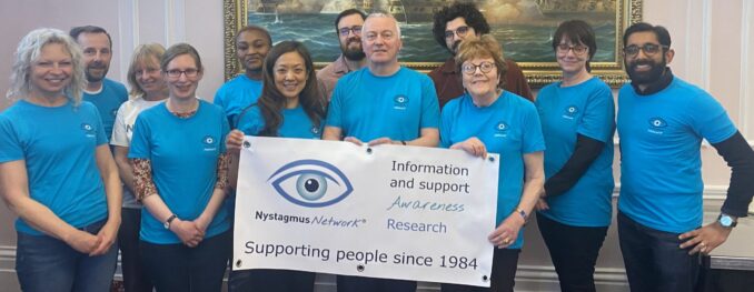 Members of the Nystagmus Network team wearing their tropical blue T-shirts hold up a banner.