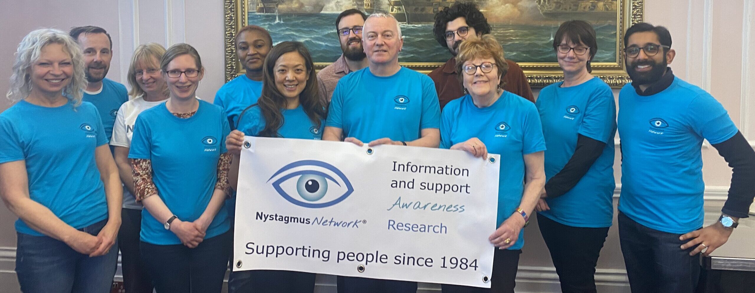 Members of the Nystagmus Network team wearing their tropical blue T-shirts hold up a banner.