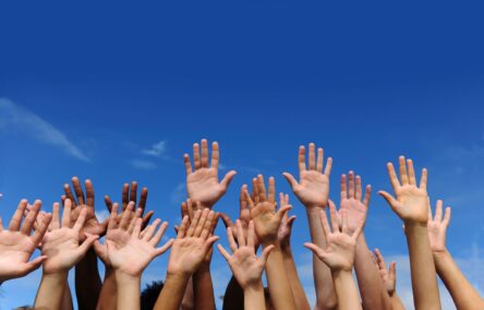 A row of hands raised in the air against a blue sky background.