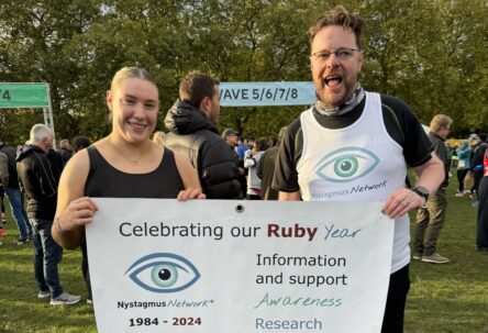 Two runners, one wearing a Nystagmus Network running vest, hold up the charity banner at the start of the Royal Parks Half Marathon.