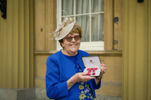 Vivien holds her MBE and smiles for the camera.