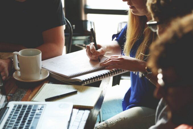 A close up of a table with laptops, pads and pens and the hands of people sitting around it.